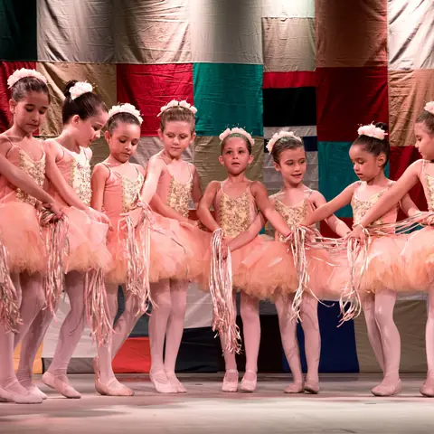 Turma de bailarinas de tutu rosê, de mãos dadas no palco.