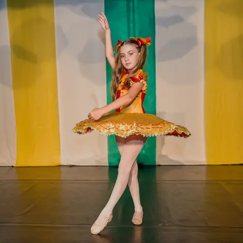 Bailarina de tutu amarelo, com um braço erguido.