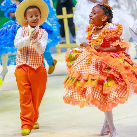 Par de quadrilha: menino de chapéu de palha e menina de vestido xadrez laranja.