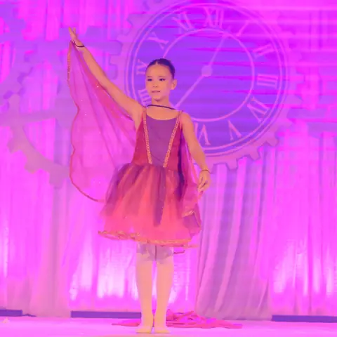 Bailarina sob luz lilás, com um grande relógio no cenário.