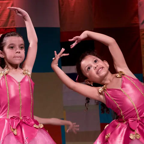 Duas bailarinas de rosa sorrindo durante a coreografia.