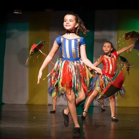 Bailarinas de saias coloridas dançando com sombrinhas.